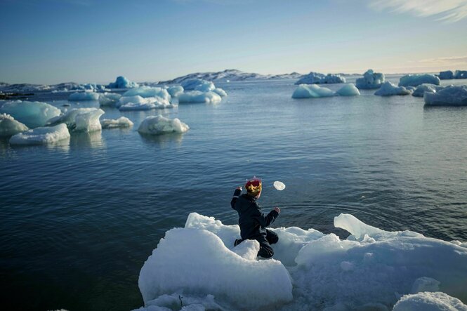 Ein Junge mit einer Krone auf dem Kopf wirft Eis ins Meer in Nuuk