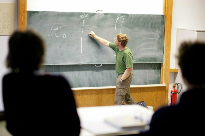 In einem Klassenraum schreibt ein Lehrer etwas an die Tafel