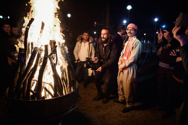 Gäste in traditioneller Kleidung stehen beim Neujahrsempfang der kurdischen Gemeinde im Hof der Landesvertretung Niedersachsen um ein Feuer herum.