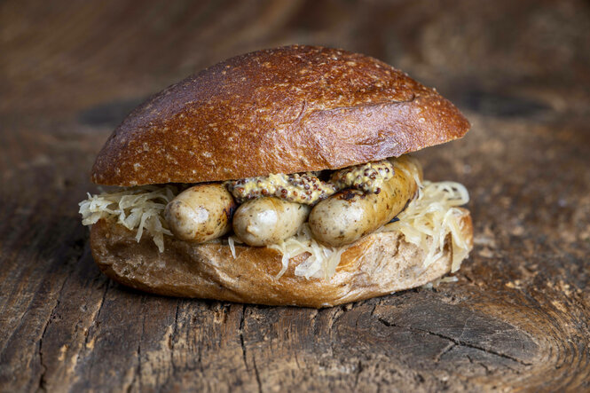 Drei gegrillte Bratwürstchen mit Sauerkraut und Senf in einem Brötchen