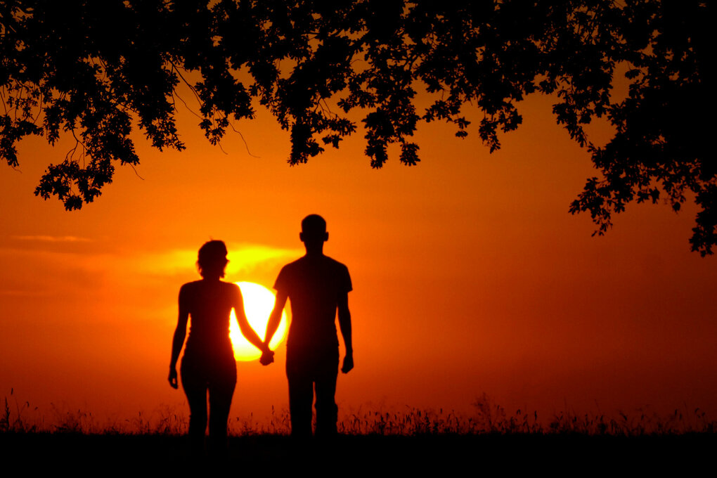 Zwei Menschen Hand in Hand vor der untergehenden Sonne