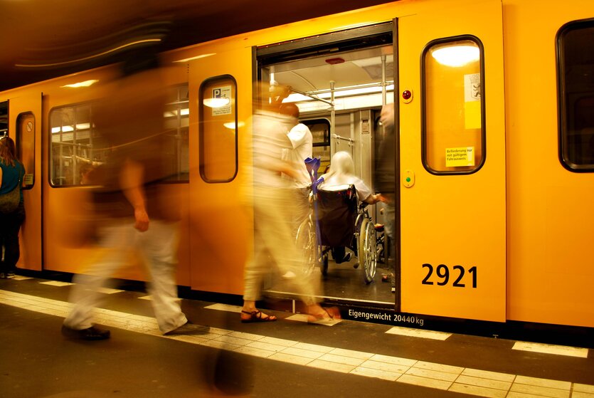 Menschen steigen in U-Bahn ein, im Inneren sitzt eine Person in einem Rollstuhl