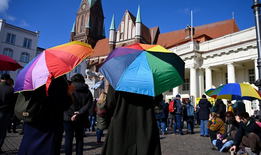 Mehrere Personen halten bunte Regenschirme bei einer Versammlung auf einem zentralen Platz in Schwerin