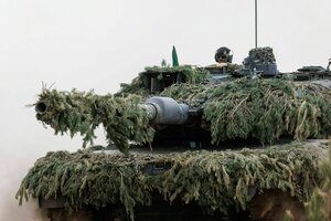 Ein Soldat sitzt auf einem Leopard 2 Kampfpanzer, der mit Tannengrün bedeckt ist