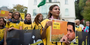 Demonstranten vor einem Gebäude mit saudischer Flagge halten ein Spruchband und ein Plakat hoch, auf dem „Free Raif“ steht.