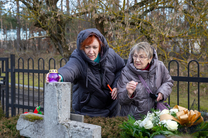 Zwei Frauen stellen eine Kerze auf ein Grabkreuz