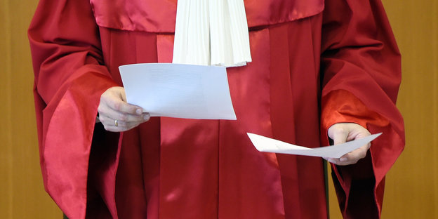Richter in roter Robe hält Zettel in der Hand