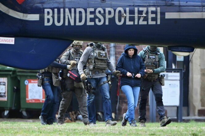 Hinter einem Helikopter mit der Aufschrift Bundespolizei wird eine Frau in Handschellen von Polizisten abgeführt