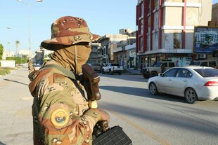 Ein bewaffneter Mann mit Hut und Gesichtsmaske steht an einer Straße und beobachtet den Verkehr