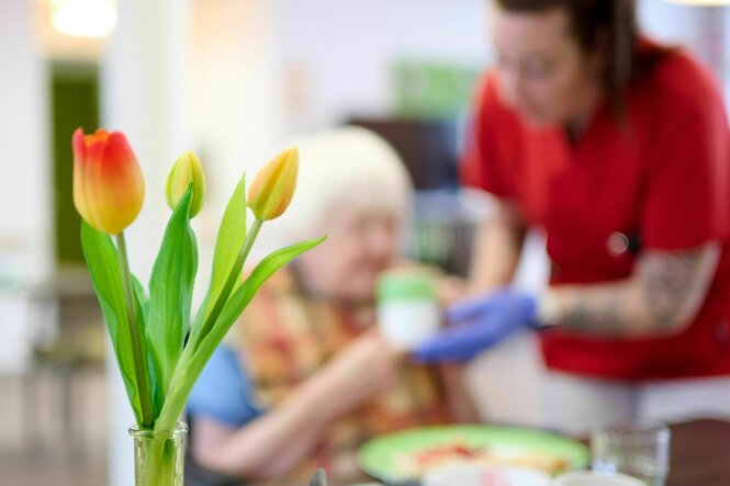 Eine Pflegekraft unterstützt eine Seniorin beim Frühstück