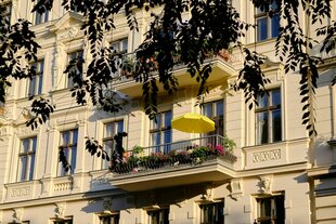 Altbaufassade im Sonnenlicht mit Balkon, auf dem ein gelber Sonnenschirm steht