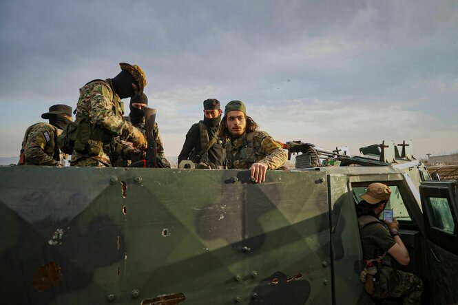 Junge syrische Soldaten in Uniform, manche vermummt, sitzen auf einem Militärfahrzeug