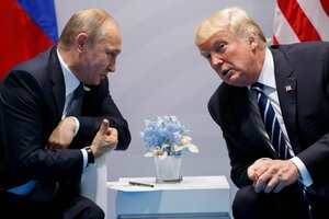 Wladimir Putin und Donald Trump unterhalten sich sitzend über einen kleinen Tisch gebäugt. Im Hintergrund sind die russische Flagge und us-amerikanische Flagge zu erkennen.