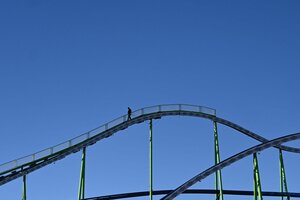 Ein Arbeiter spaziert vor blauem Himmel über eine Achterbahn.