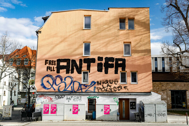 Auf einer Hauswand sind verschiedene Graffiti zu sehen. Am auffälligsten sind die Worte 'FREE ALL ANTIFA'