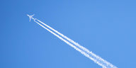 Flugzeug mit Kondensstreifen vor blauem Himmel.
