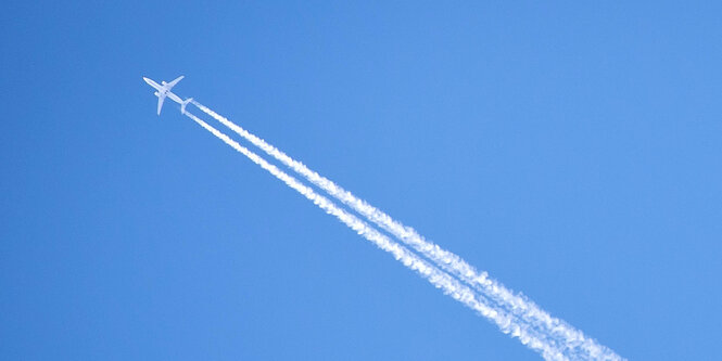 Flugzeug mit Kondensstreifen vor blauem Himmel.