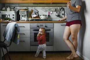 Eine Frau in kurzen Hosen steht mit ihrem Kleinkind an der Küchenzeile, ihr Kopf ist nicht zu sehen