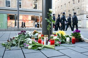 Kerzen und Blumen liegen an einem Pfahl in der Innenstadt von Mannheim, im Hintergrund eine Gruppe Polizist:innen