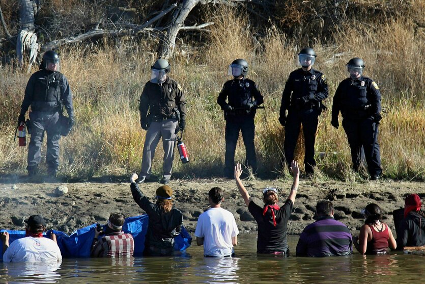 Menschen in T-Shirts stehen in einem Fluss und schauen zu Menschen in Uniform auf