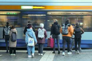 Menschen stehen an der Haltestelle und stehen vor einer Straßenbahn die gerade einfährt