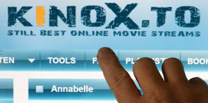 Ein Abbild der Startseite von Kinox.to, mit einer Hand im Vordergrund.