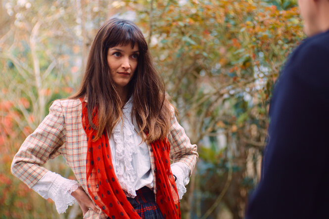 Niki de Saint Phalle (Charlotte Le Bon) steht selbstbewusst im Freien vor einem Mann.