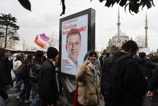 Demonstrierende laufen an einem Plakat von Ekrem Imamoglu vorbei