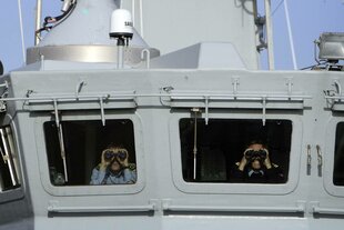 Personen mit Ferngläsern auf einem Militärschiff.