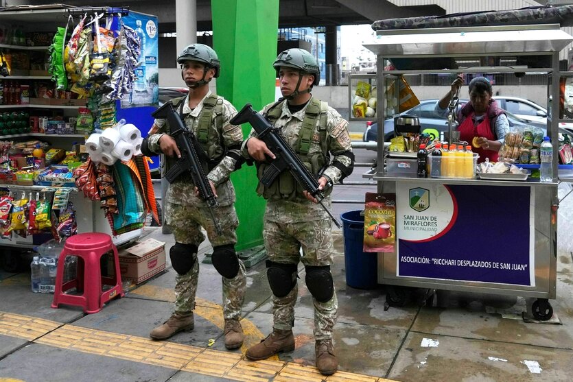 Zwei bewaffnete Soldaten stehen an einer Fußgängerzone in Lima, hinter ihnen Verkaufsstände mit Limonade und Süssigkeiten