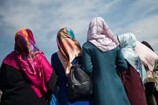 Rückenansicht von muslimischen Frauen mit Kopftuch, sie stehen im Feien, der Himmel ist blau und die Sonne scheint