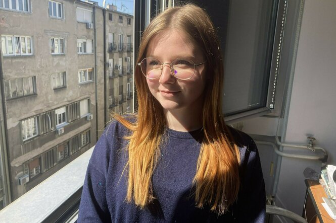 Eine Studentin mit blauem Pullover steht an einem Fenster