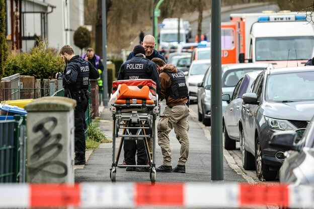 Poliziststen stehen auf einem Gehweg, neben einer fahrbaren Krankenbahre. Im Hintergrund steht ein Rettungsfahrzeug