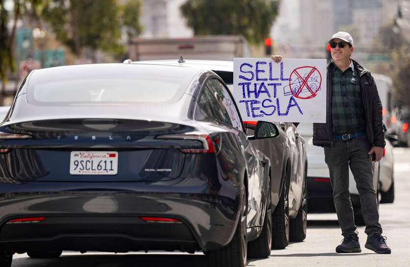 Ein Demonstrant hält ein Schild mit der Aufschrift "SELL THAT TESLA" vor einem Tesla-Fahrer während einer Kundgebung vor einem Tesla-Händler in San Francisco.