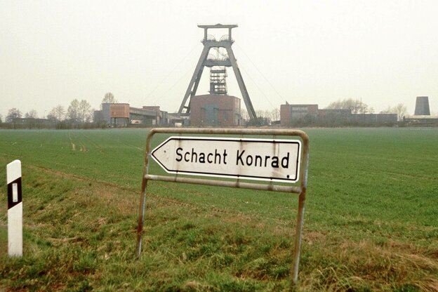Ein Hinweisschild, Aufschrift „Schacht Konrad“, im Hintergrund ein Förderturm