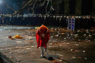 Ein Mann mit der türkischen Flagge auf dem Rücken steht bei einer Kundgebung gegen die Verhaftung von Istanbuls Bürgermeister Ekrem Imamoglu in Istanbul, Türkei, vor einer großen Zahl Polizisten