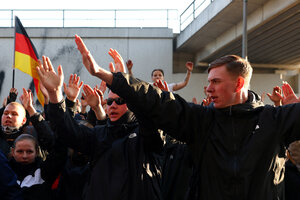 Schwarz gekleidete Neonazis recken die Hände, einer zeigt den Hitlergruß