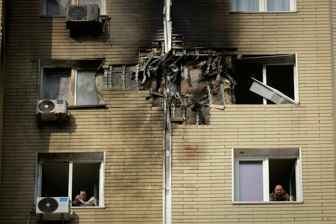 Ein Bewohner blickt aus dem Fenster seiner Wohnung in einem mehrstöckigen Haus, das bei einem nächtlichen russischen Drohnenangriff in Kiew beschädigt worden ist.