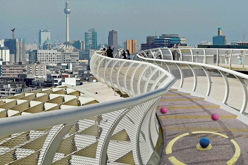 Montage - das Bild zeigt die Skyline von Berlin mit Fernsehturm, den Skywalk aus Sevilla, der ein helles geschwungenes Geländer hat und auf dem Boden eine Minigolfanlage