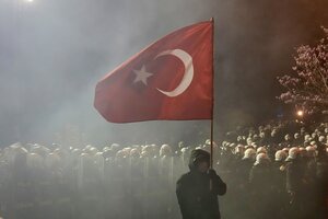 Ein Mann steht mit Türkeiflagge vor einem großen Polizeiaufgebot