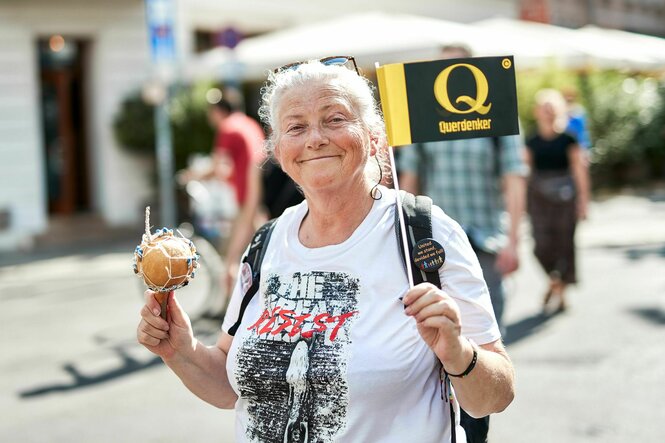 Eine alte Frau hält ein Fähnchen mit einem "Q" für Querdenker