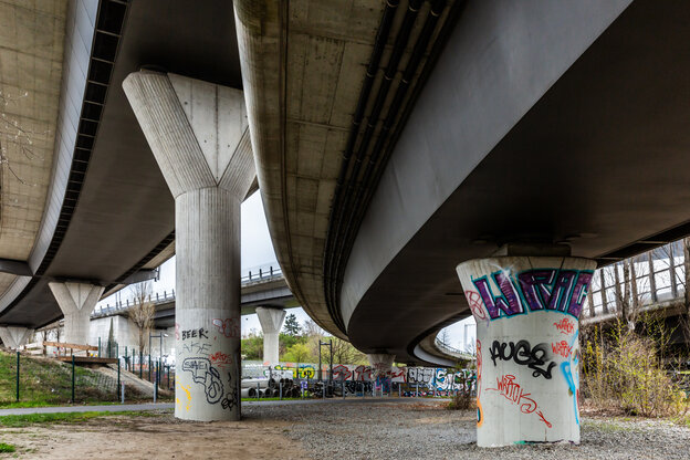 Das Bild zeigt die massiven Betonstützpfeiler einer Stadtautobahnbrücke von unten und einen Teil der Fahrbahn.