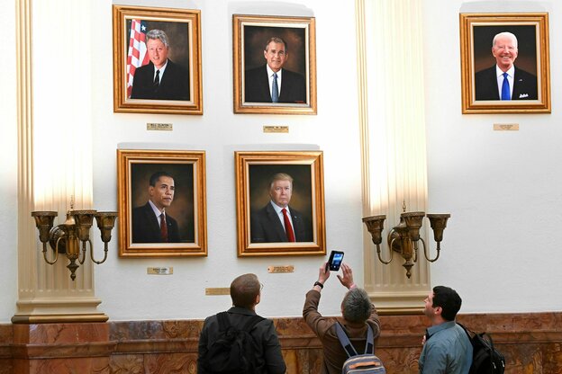 Portätgemälde der letzten fünf Präsidenten der USA hängen an einer Wand, drei Personen blicken hinauf, eine macht ein Foto mit dem Handy