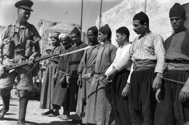 Einige Männer in traditionellen Gewändern werden von einem britischen Soldaten mit aufgepflanztem Bajonett bewacht