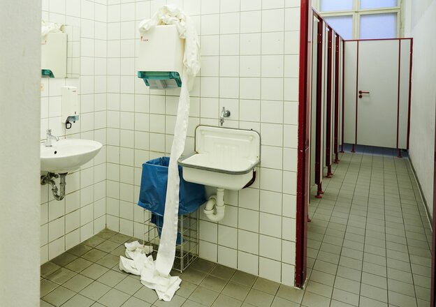 In einer Berliner Schultoilette fällt die benutzte Handtuchrolle vom Handtuchspender auf den Boden.