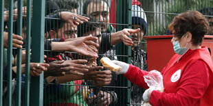 Eine Rot-Kreuz-Helferin gibt Flüchtlingen einzelne Brotscheiben durch einen Zaun