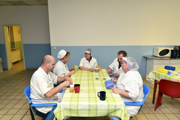 Eine Gruppe von fünf Personen in sauberer Fleischreikleidung sitzen am Kaffeetisch und machen Pause