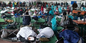 Flüchtlinge sitzen und liegen auf Feldbetten
