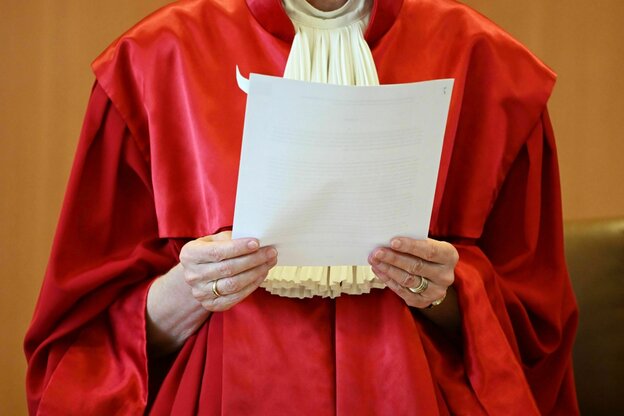Eine Person in roter Robe hält ein Dokument in den Händen