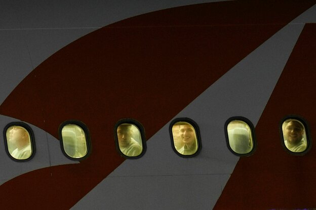 Nahaufnahme von der Seite eines Flugzeugs, durch die Fenster des Flugzeugs sehen wir einzelne Gesichter, teils lächeln sie, teils neutral- ängstlich.